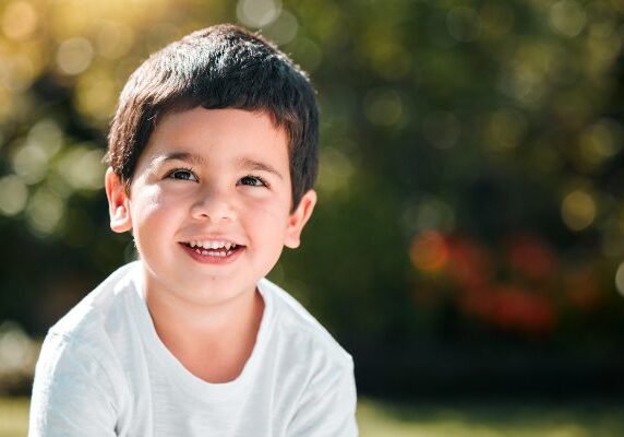 Boy sitting on the grass in a park, wearing a t-shirt and at the camera