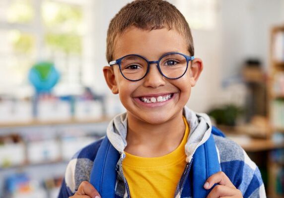 Boy wearing glasses and a backpack, with a bright smile on his face
