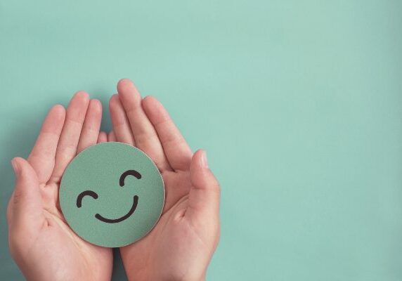 Person holding a green smiley face in their hands against a blue background