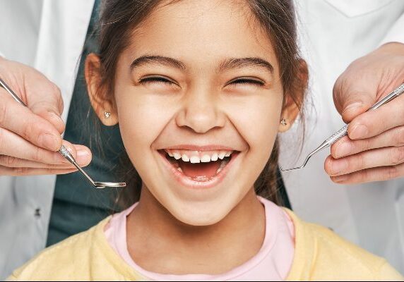 Girl with a big smile on her face, being examined by a dentist