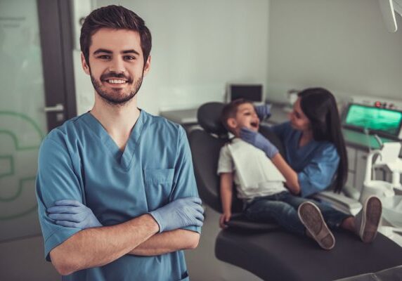 Man standing in front of a child in a dentist's chair, with a woman sitting beside him