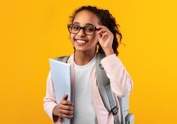 Girl wearing glasses and a backpack, holding a book in her hand
