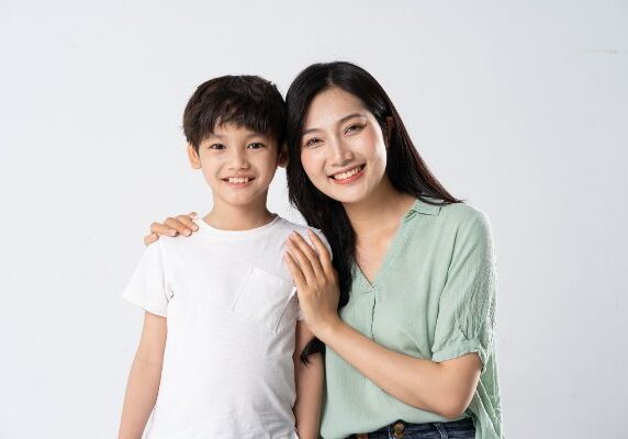 Woman and a boy standing side by side, both with smiles on their faces, against a white background