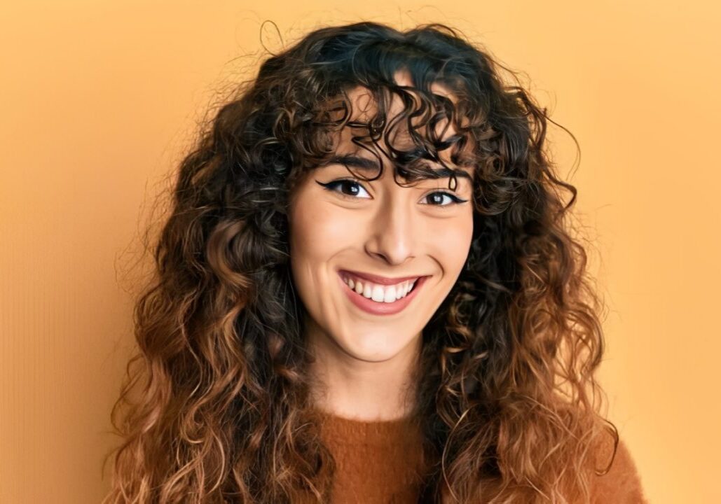 Woman with long curly hair at the camera against a yellow background
